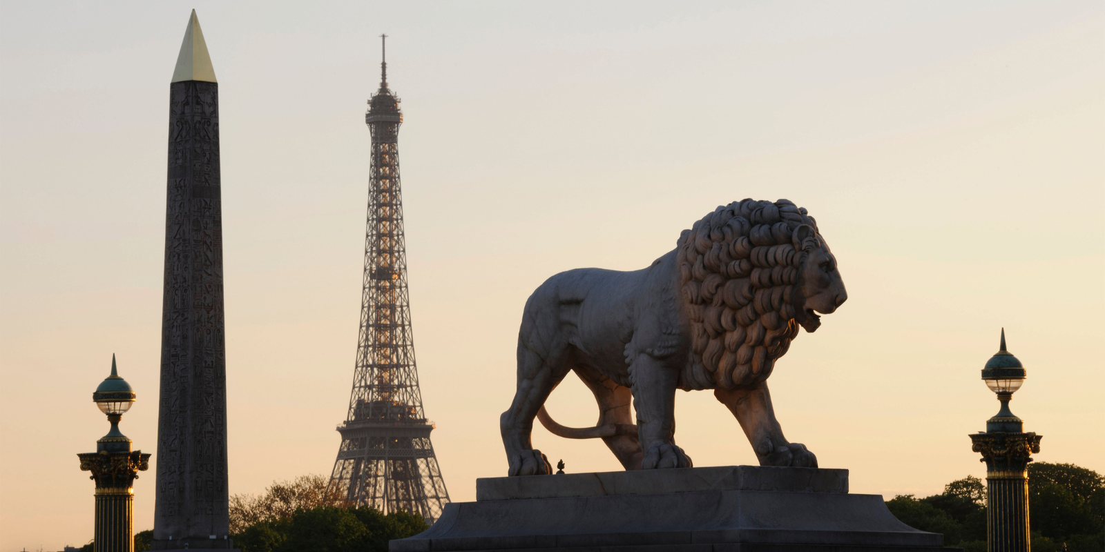Silhouette of a lion statue with the Eiffel Tower in the background during sunset.