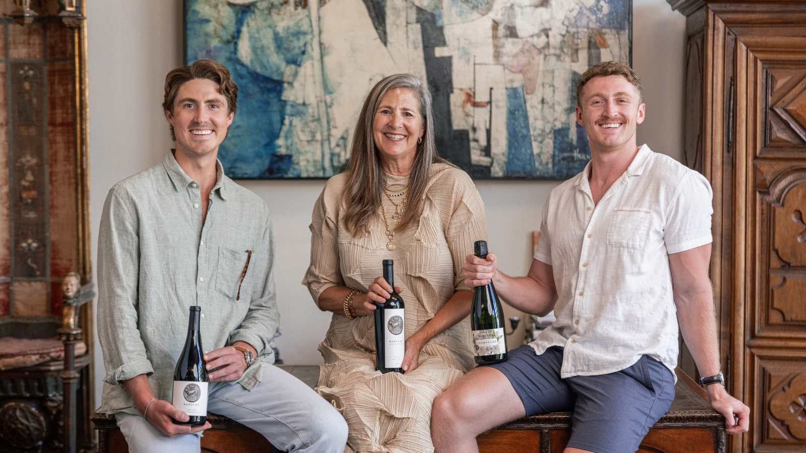 Three people holding wine bottles in a room with decorative elements